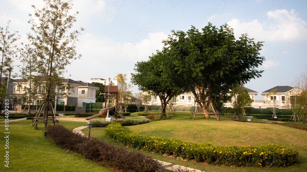 well-maintained garden in a residential area. The garden is adorned with lush green grass, blooming flowers, and mature trees. There are also some structures that appear to be supporting young trees. well-maintained garden in a residential area. The garden is adorned with lush green grass, blooming flowers, and mature trees. There are also some structures that appear to be supporting young trees.