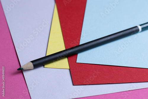 Black pencil sitting on several sheets of colored paper.