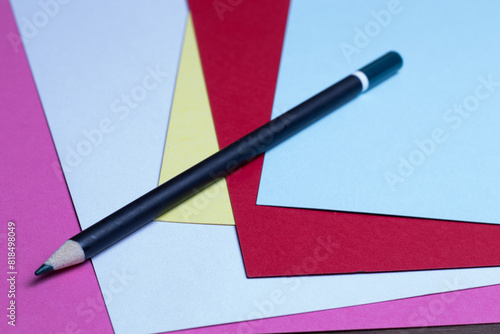 Black pencil sitting on several sheets of colored paper.