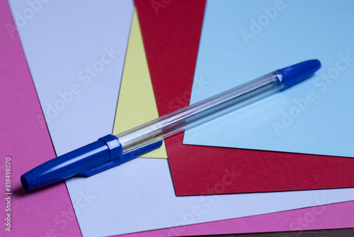 Generic blue ballpoint pen sitting on several sheets of colored paper.