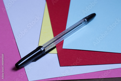 Generic black ballpoint pen sitting on several sheets of colored paper.