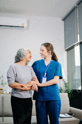 Young nurse helping elderly woman walk in the room, holding his hand, supporting. Treatment and rehabilitation after injury