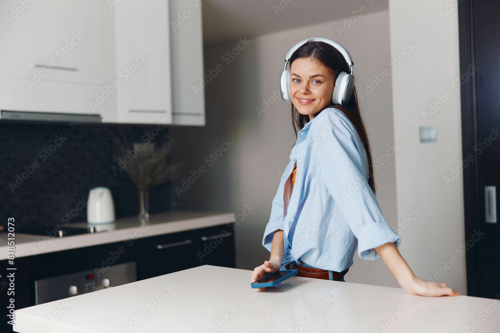 Young woman standing on kitchen counter, wearing headphones, holding phone in hand, enjoying music Young woman standing on kitchen counter, wearing headphones, holding phone in hand, enjoying music