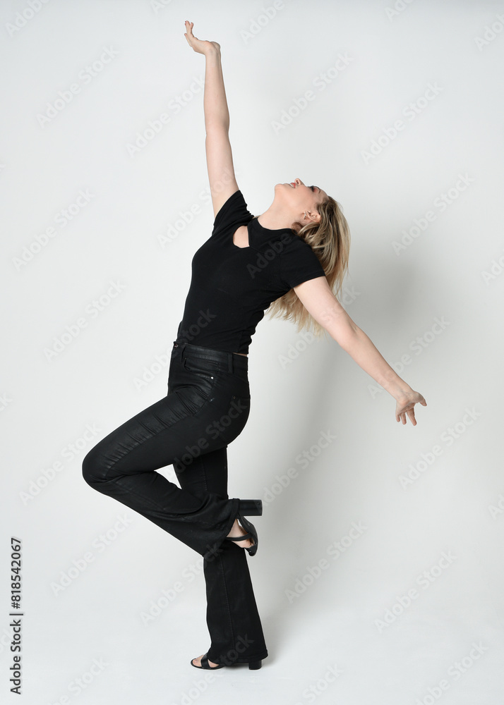 Naklejka premium Full length portrait of beautiful blonde woman wearing modern black shirt and leather pants. Confident standing pose with gestural hands presenting, silhouetted on white studio background.