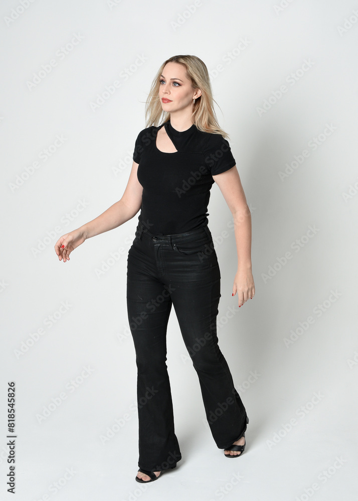 Full length portrait of beautiful blonde woman wearing modern black shirt and leather pants. Confident standing pose with gestural hands presenting, silhouetted on white studio background. Full length portrait of beautiful blonde woman wearing modern black shirt and leather pants. Confident standing pose with gestural hands presenting, silhouetted on white studio background.