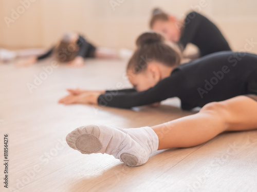 Girls ballerinas stretch while lying in a wide fold. 