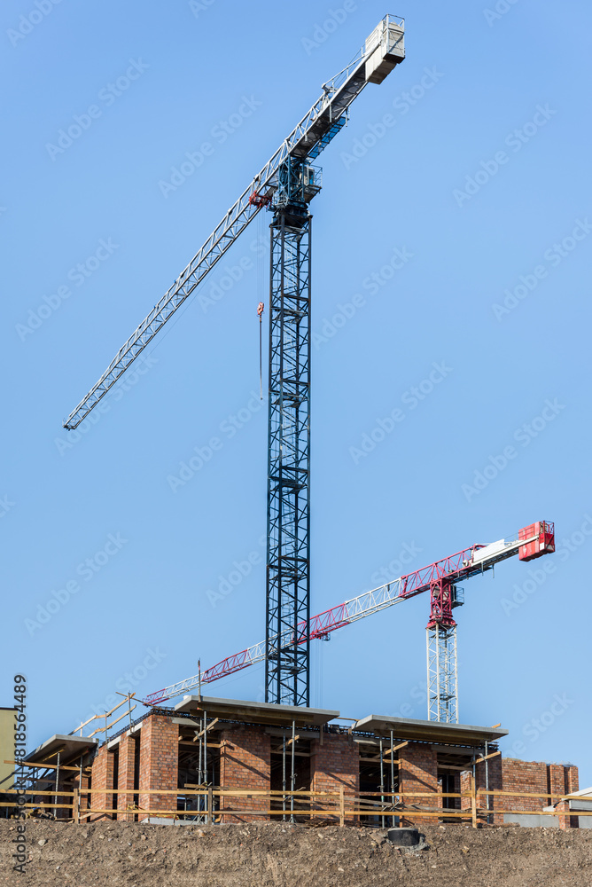A Pair Of Building Tower Cranes Working In Construction Site On Blue Sky Background A Pair Of Building Tower Cranes Working In Construction Site On Blue Sky Background