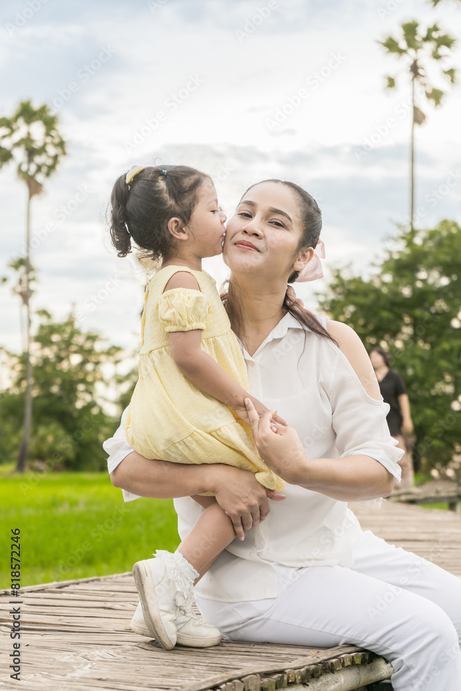 Asian mother and daughter express their love for each other by kissing her mother on the cheek on a wooden bridge in a rice field. Asian mother and daughter express their love for each other by kissing her mother on the cheek on a wooden bridge in a rice field.