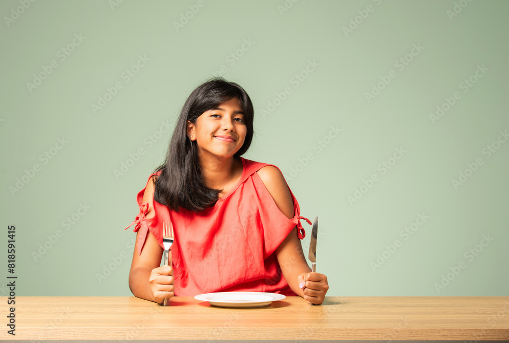 Asian Indian adorable girl child holding empty ceramic plate with happy expressions, sitting on table Asian Indian adorable girl child holding empty ceramic plate with happy expressions, sitting on table