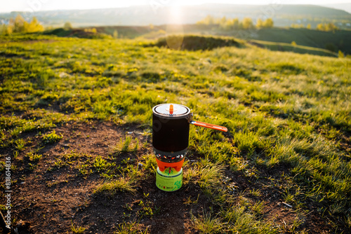 Outdoor cooking pot on portable stove at stunning sunrise landscape. Culinary equipment for camping, hiking, and outdoor adventures in nature. Enjoy breakfast in the wilderness