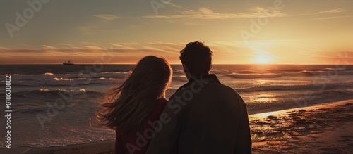 A couple at sunset on the beach in winter photographed from the side with them looking away The image allows for copy space