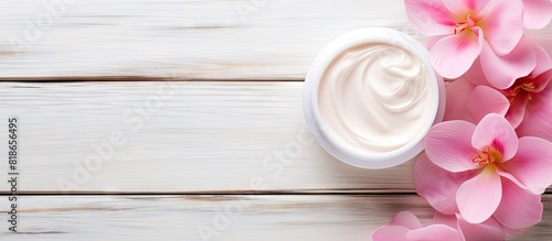 A cosmetic cream with pink flower petals sits on a white wood table creating a beautiful composition in the copy space image