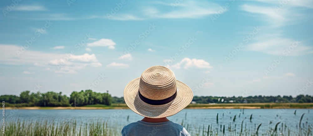 Obraz premium Copy space image of a boy wearing a hat viewed from behind with a serene summer lake as the backdrop