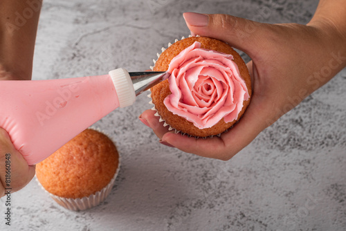 Female hands decorating a cupcake with cream cheese frosting. Decoration using a piping bag. photo