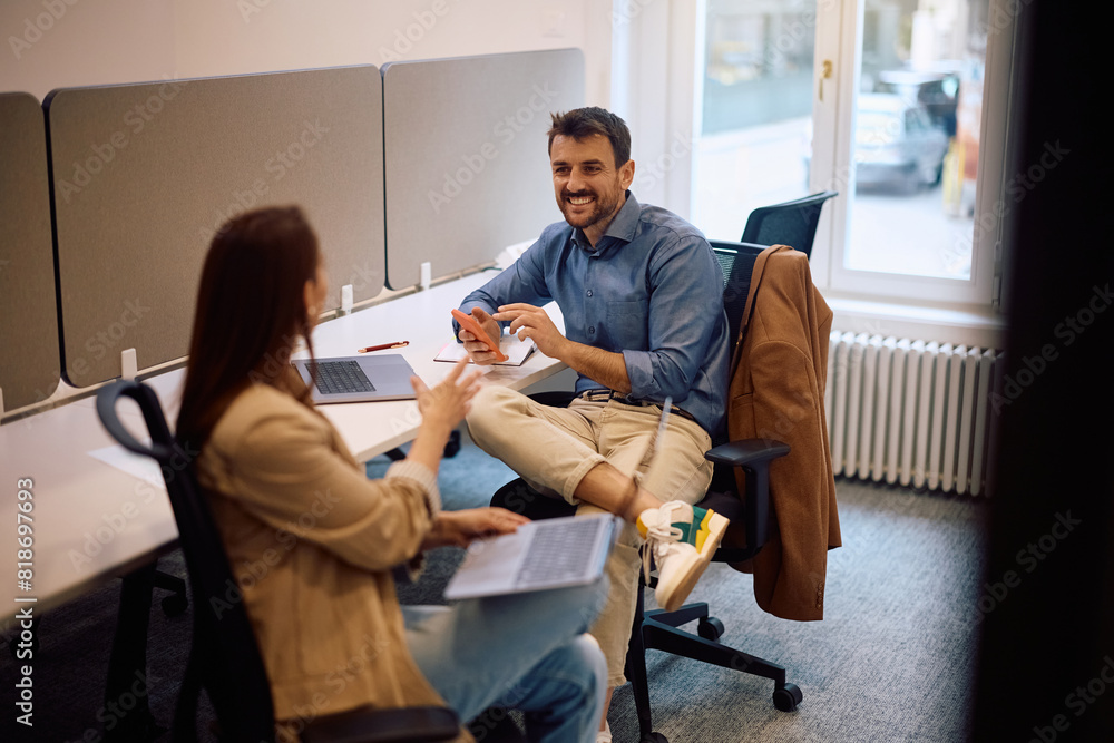 Happy entrepreneur using cell phone while talking to female colleague in office. Happy entrepreneur using cell phone while talking to female colleague in office.
