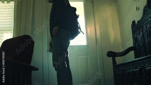 Young man in casual clothes and backpack opening the door and entering the house