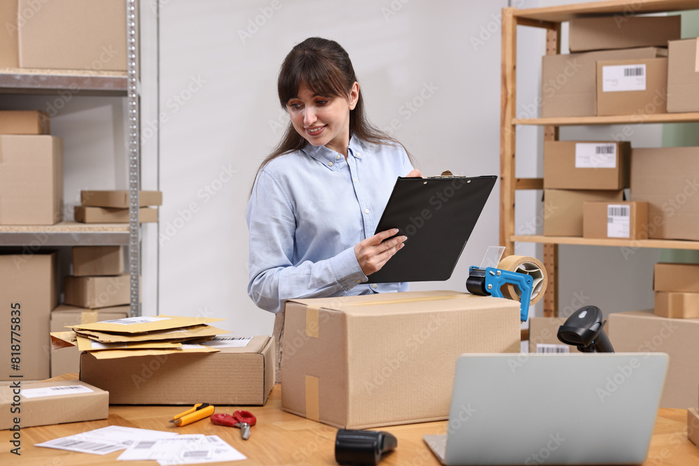 Parcel packing. Post office worker with clipboard writing notes at wooden table indoors Parcel packing. Post office worker with clipboard writing notes at wooden table indoors