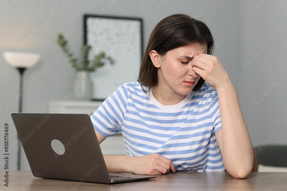 Overwhelmed woman sitting with laptop at table indoors Overwhelmed woman sitting with laptop at table indoors