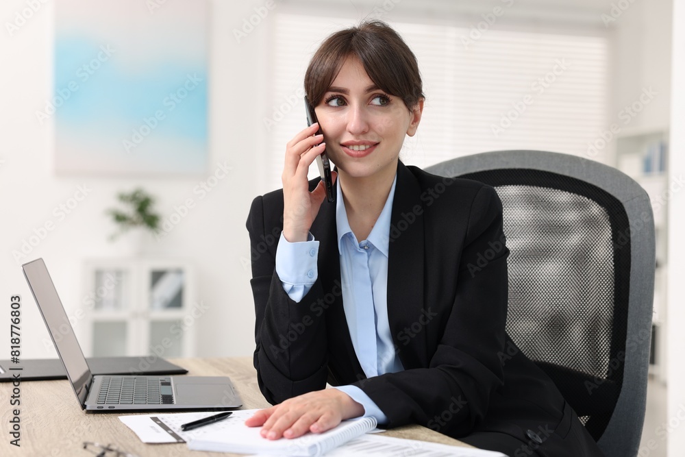 Smiling secretary talking by smartphone at table in office Smiling secretary talking by smartphone at table in office