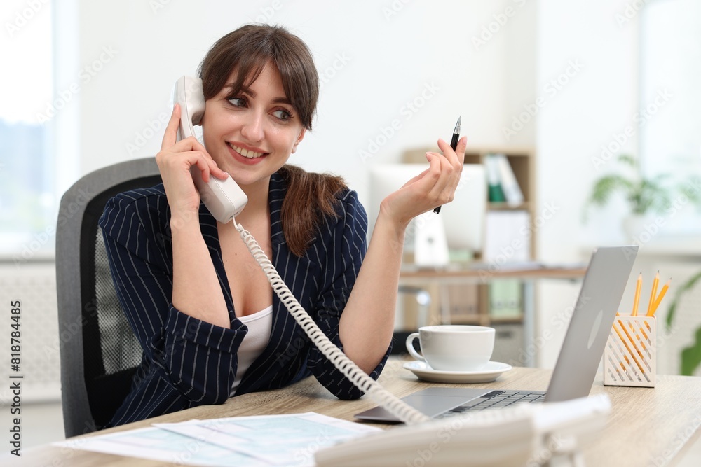 Smiling secretary talking on telephone at table in office