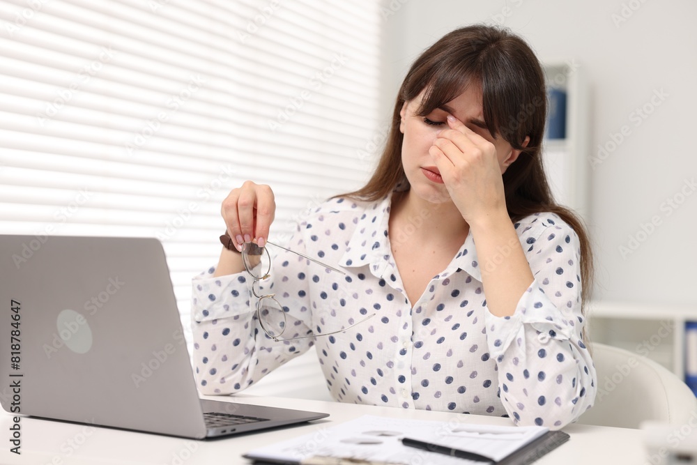 Overwhelmed woman sitting at table with laptop in office Overwhelmed woman sitting at table with laptop in office
