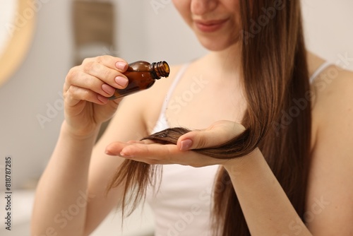 Woman applying oil hair mask indoors, closeup photo