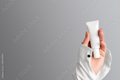 Hand of a girl in a white shirt with a tube of white cream on a gray background with copy space