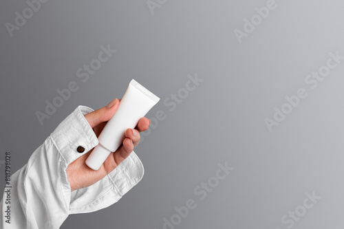 Hand holding a tube with a cosmetic product on a gray background