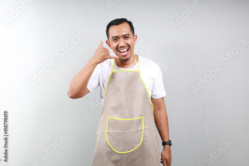 Asian man barista bartender barman employee in brown apron white t-shirt work in coffee shop doing phone gesture like says call me back isolated on gray background Small business startup concept photo