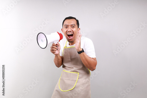 Asian male housekeeper chef cook baker man wear apron hold in hand megaphone scream announces discounts sale Hurry up isolated on gray background studio Cooking food concept