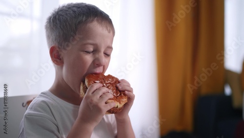 kid preschool boy eats hamburger a lifestyle breakfast at recess. happy family fast food kid dream concept. child son eating hamburger fast food sitting at a table by the window