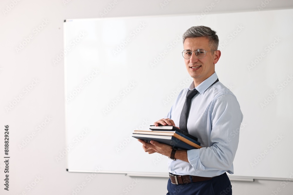 Teacher with notebooks near whiteboard in classroom Teacher with notebooks near whiteboard in classroom