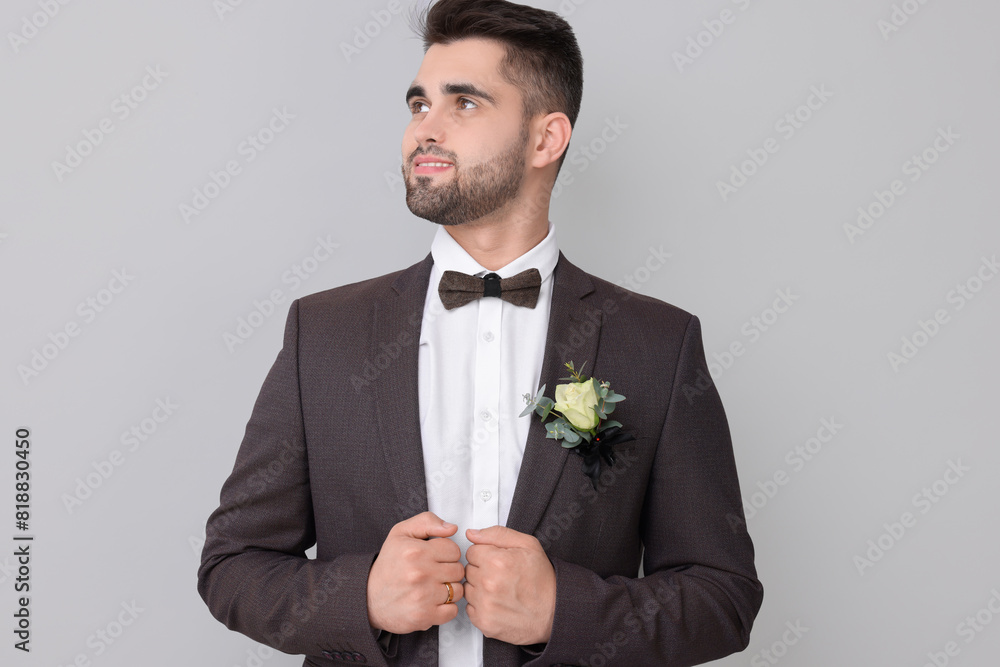 Handsome young groom with boutonniere on light grey background. Wedding accessory Handsome young groom with boutonniere on light grey background. Wedding accessory