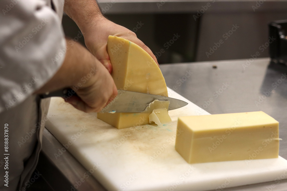 Unrecognizable person cutting cheese on a board in the kitchen of a restaurant Unrecognizable person cutting cheese on a board in the kitchen of a restaurant