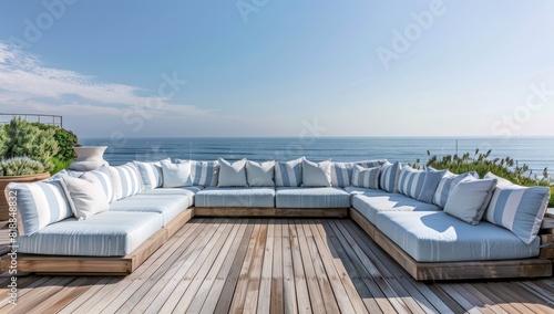 A large, light blue and white striped outdoor sofa set on the wooden deck of an oceanfront home in Malibu with panoramic sea views under a clear sky