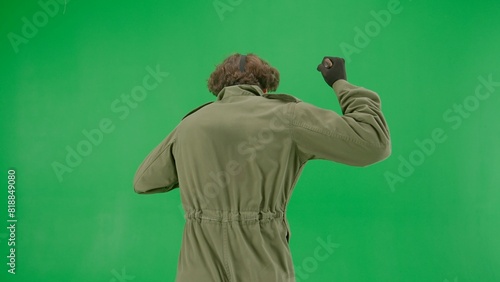 Maniac in hockey mask and jumpsuit running and waving a large sharp knife. An unrecognizable man in the terrifying guise of Jason Voorhees on a green screen chromakey. Halloween, horror. Back view.
