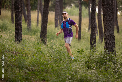A man is running through a forest wearing a purple shirt and blue backpack