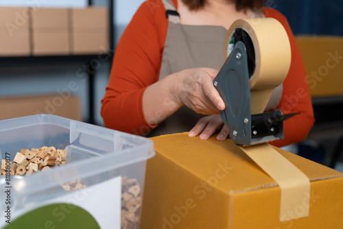 A woman using kraft paper tape to seal a cardboard box in a home-based business, highlighting eco-friendly packaging and sustainable practices in small business operations
