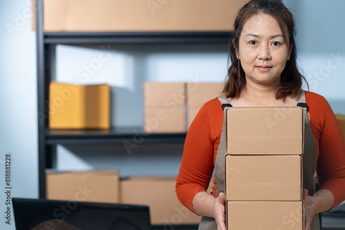 A small business owner stands confidently in her home workspace, holding cardboard boxes, The business focuses on sustainable shipping practices using easily recyclable materials