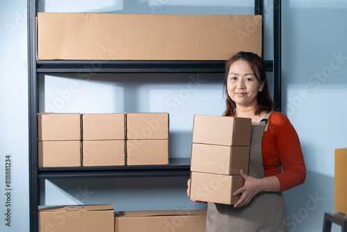 A small business owner stands confidently in her home workspace, holding cardboard boxes, The business focuses on sustainable shipping practices using easily recyclable materials