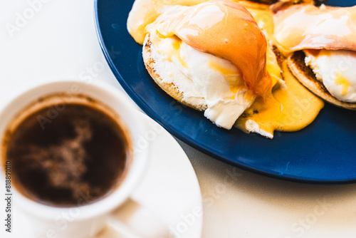 Egg Benedict with salmon and hollandaise sauce on a blue plate with a cup of freshly brewed coffee. selected focus. Concept: healthy breakfast