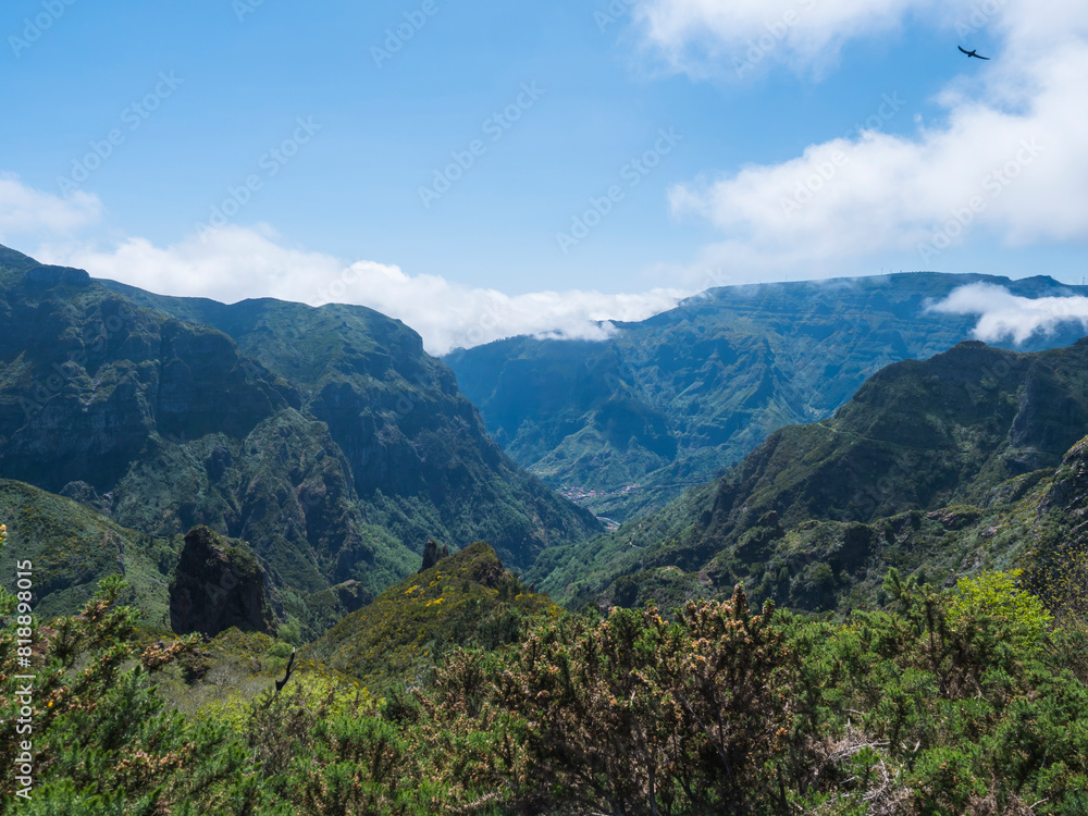 Fototapeta premium View of green hills, mountain landscape in clouds at blue sky. and lush vegetation at hiking trail PR12 to Pico Grande one of the highest peaks in the Madeira, Portugal