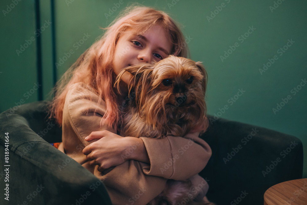 A beautiful little girl hugs a Yorkshire terrier while sitting on a chair. A beautiful little girl hugs a Yorkshire terrier while sitting on a chair.