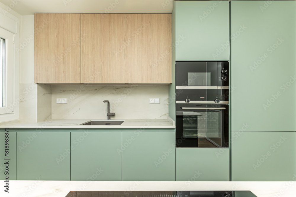 Front image of a modern design open kitchen with pastel green furniture, white circular decorative hood, columns of integrated appliances and marble backsplash Front image of a modern design open kitchen with pastel green furniture, white circular decorative hood, columns of integrated appliances and marble backsplash