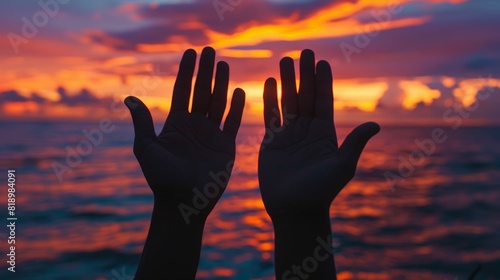 Two hands reaching out towards the ocean, with the sun setting in the background