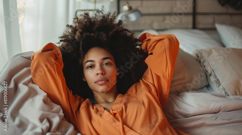 serene young africanamerican woman relaxing on bed in orange pajamas indoor bedroom scene photo