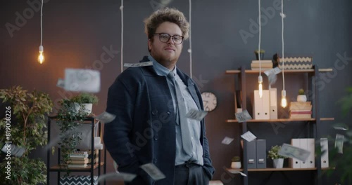 Portrait of wealthy businessman throwing dollar banknotes looking at money standing in dark office in evening. Finance and business concept.