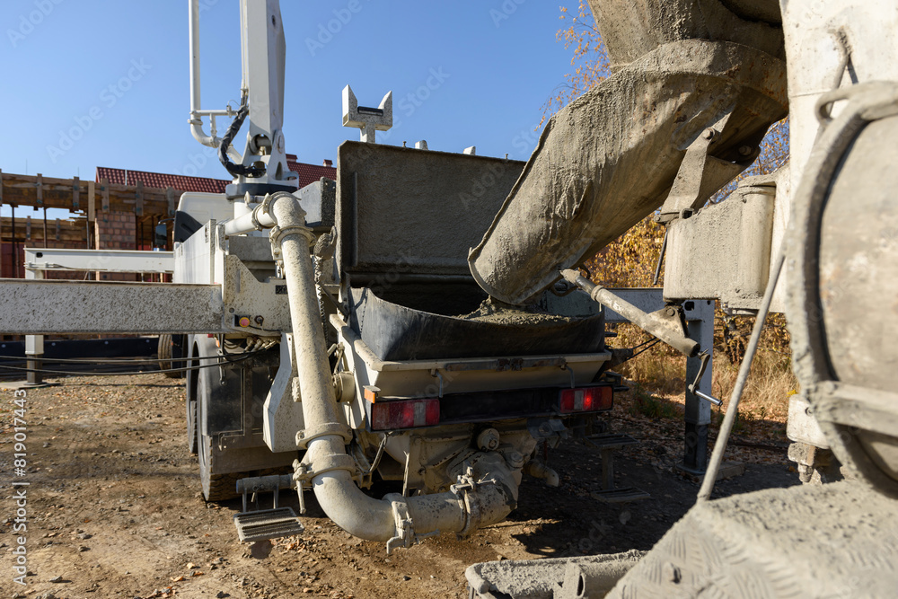 Pouring concrete at a construction site. The concrete is poured into the loading hopper of the concrete pump from the concrete mixer guide chute. The process of pouring the foundation in a building. Pouring concrete at a construction site. The concrete is poured into the loading hopper of the concrete pump from the concrete mixer guide chute. The process of pouring the foundation in a building.