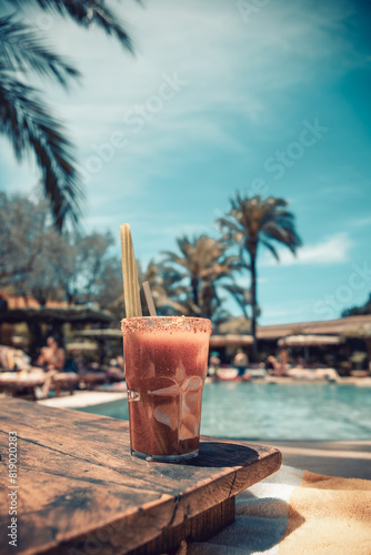 Close up shot of a Bloody Mary cocktail with a celery stick inside and crushed spices on the glass' edge at the pool, in a sunny afternoon in Ibiza. Vacation mood, relax, pool party vibes.