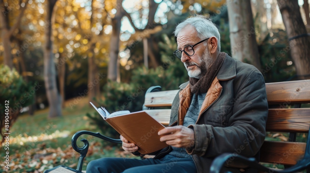 Confident mature man in smart casual wear holding notepad and looking at it while sitting on a wooden bench in park Confident mature man in smart casual wear holding notepad and looking at it while sitting on a wooden bench in park